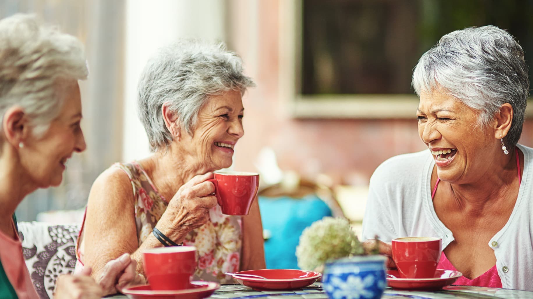 Three older women laughing over coffee