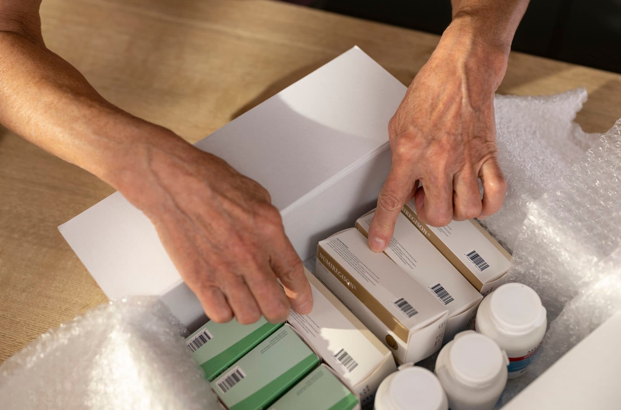 Hands packing medicine bottles into a shipping box